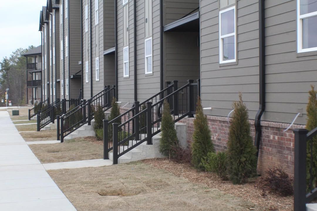 Row of townhouses with black railings, small bushes, and sidewalk.