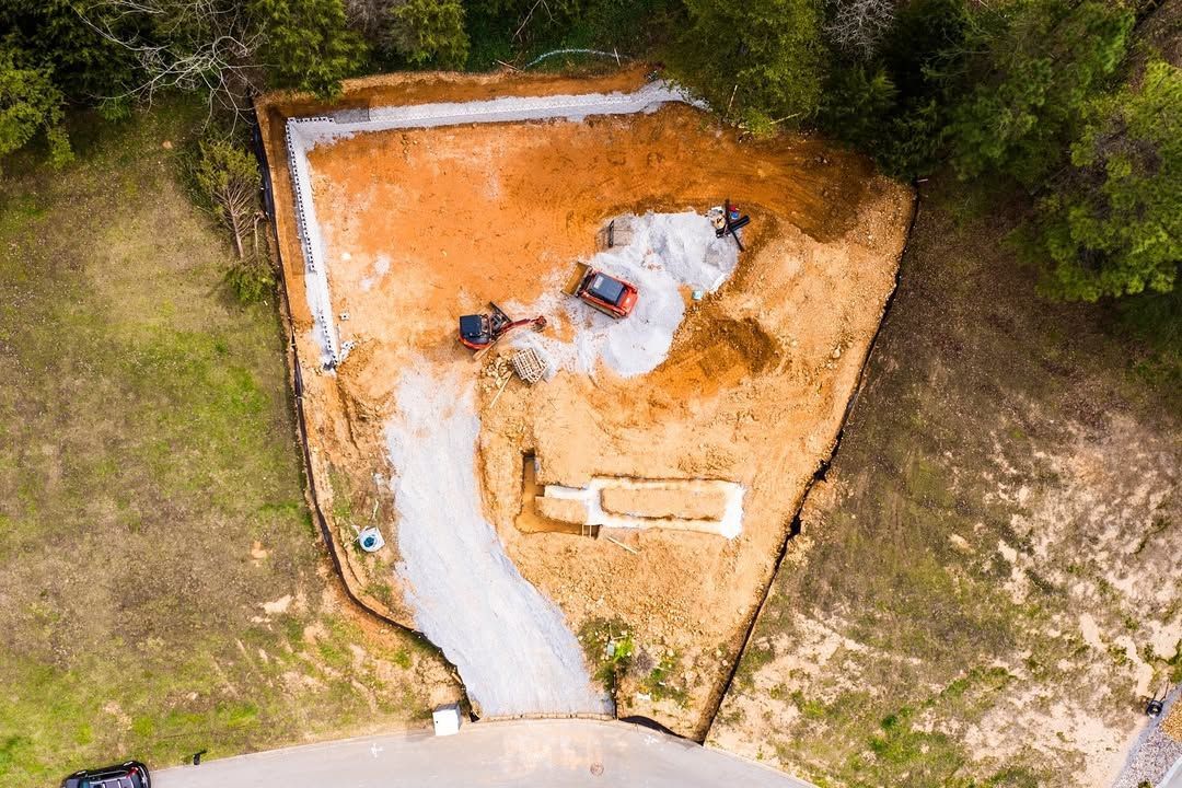Overhead view of a construction site: excavated area, gravel driveway, machinery, and piles of dirt.
