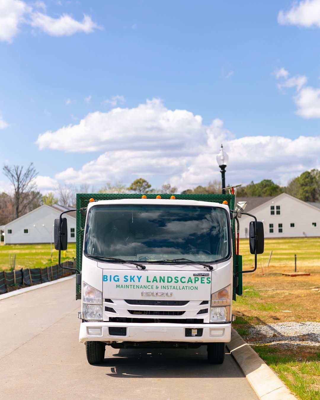 White Big Sky Landscapes truck parked on a street with houses and a blue sky in the background.