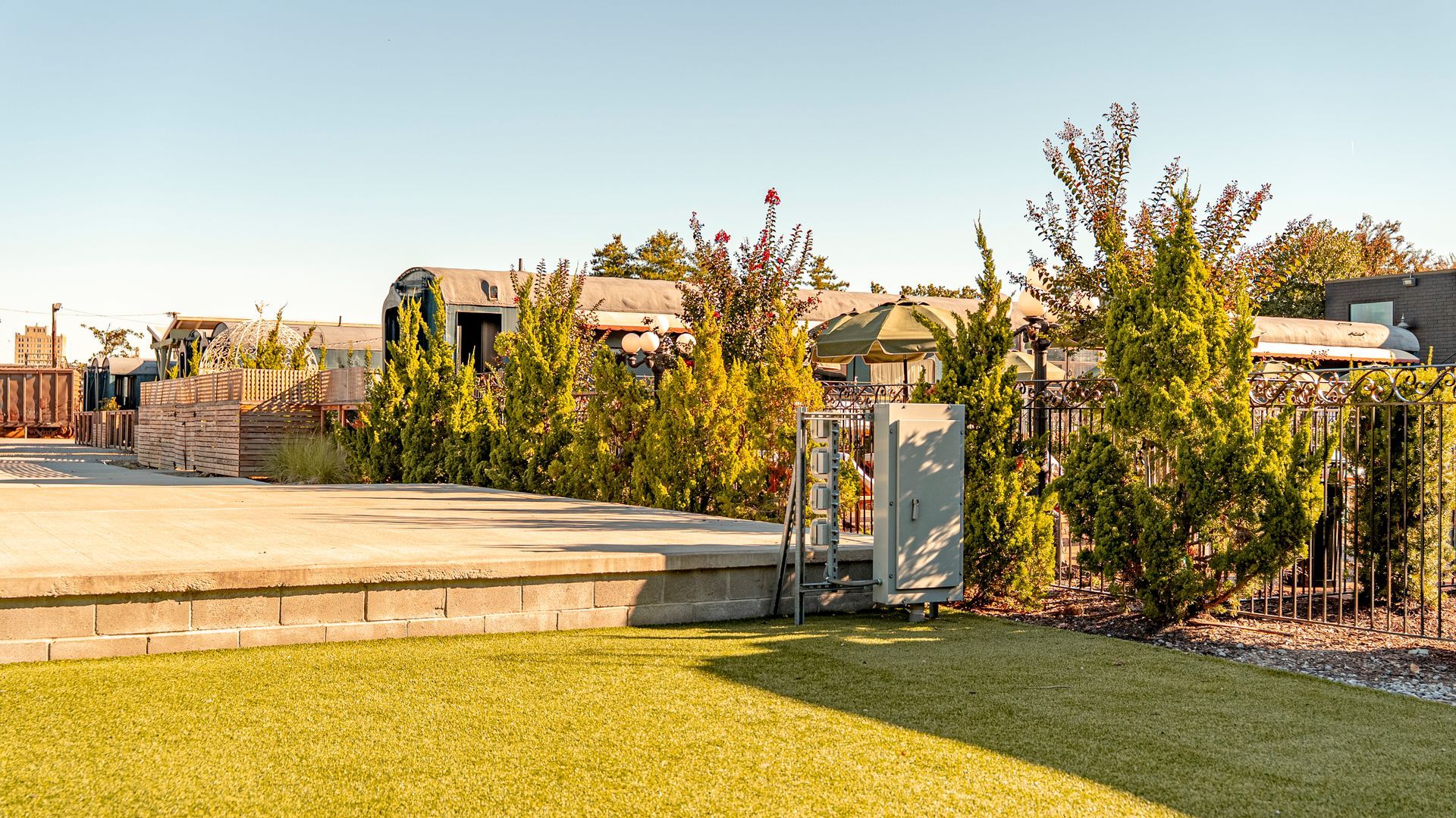 Lawn and concrete patio in foreground; trees, buildings, and clear sky in background.