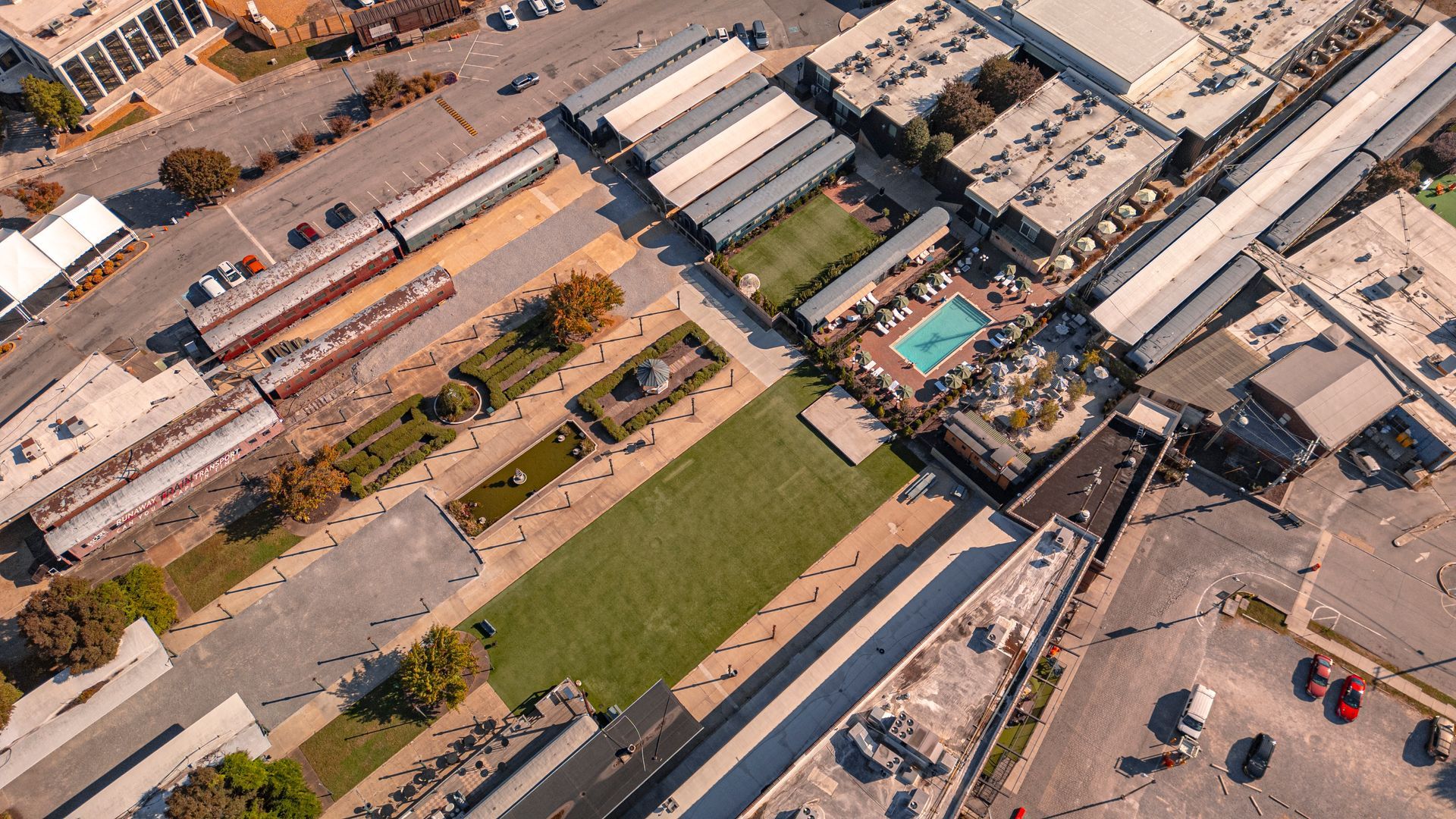 Aerial view of a plaza with buildings, a pool, a grassy area, and people.
