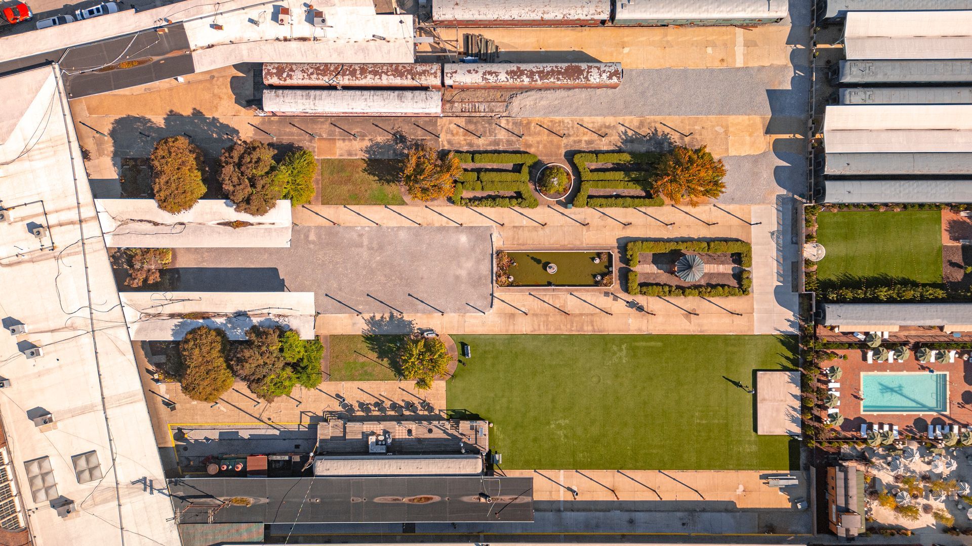 Overhead view of a plaza with trees, lawns, landscaping, and train cars, including a swimming pool.