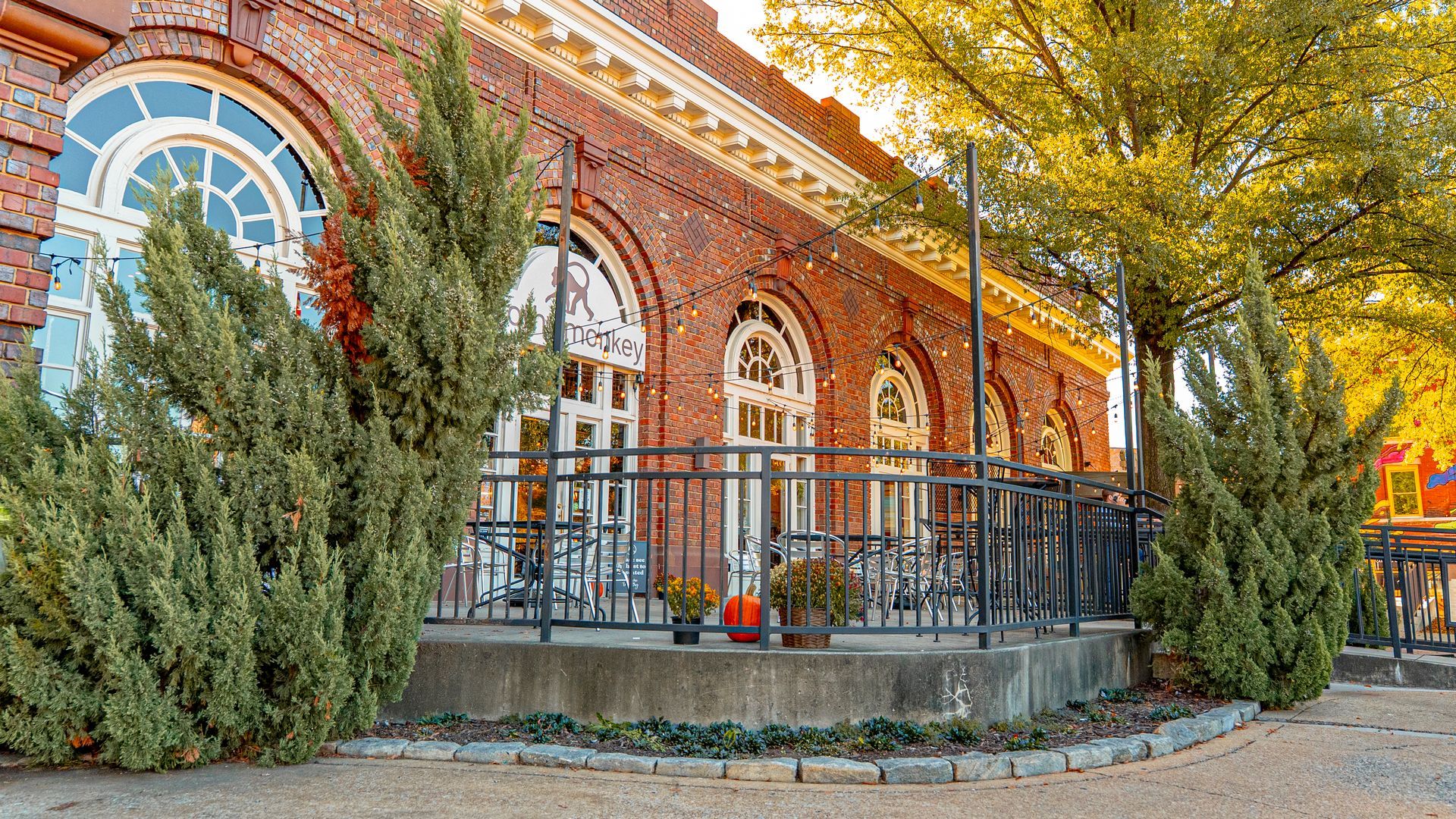 Red brick building with arched windows and a small patio, shrubs in front.