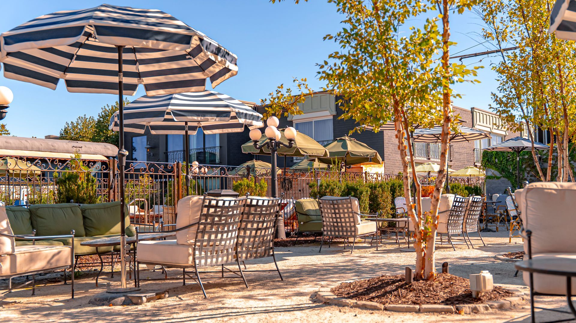 Outdoor restaurant patio with striped umbrellas, tables, chairs, and foliage.