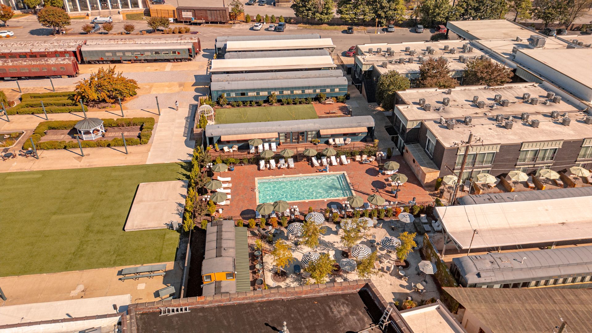 Aerial view: hotel complex with pool, train cars, and buildings, set in a sunny, outdoor area.