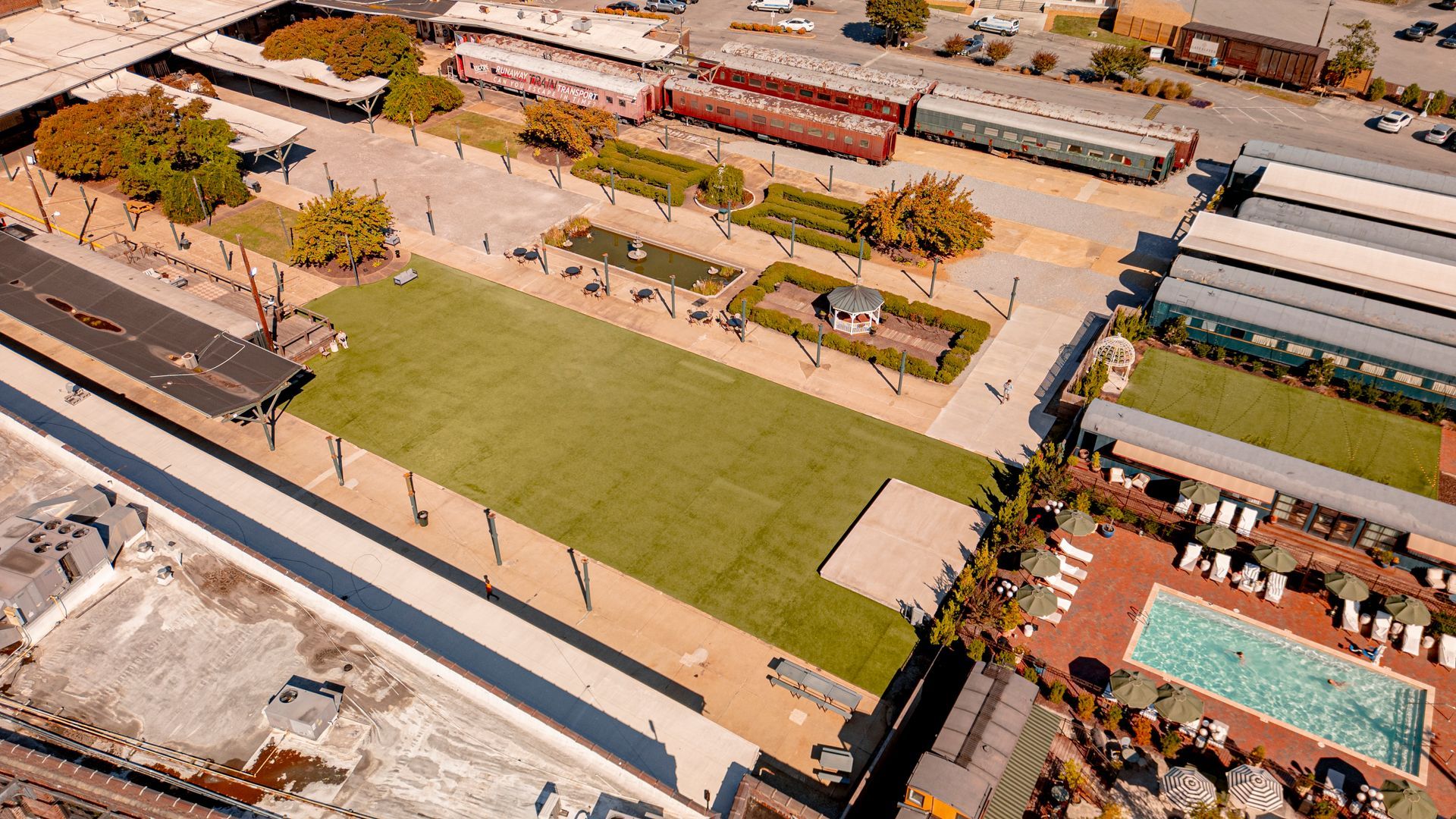 Aerial view of a complex with train cars, a green lawn, buildings, and a swimming pool.