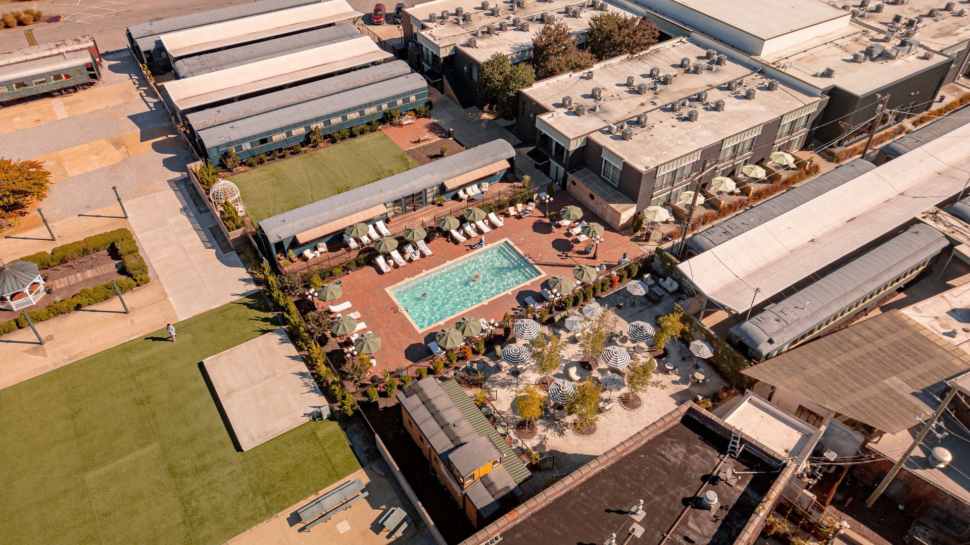 Aerial view of a resort with a pool, lounge chairs, buildings, and green spaces.