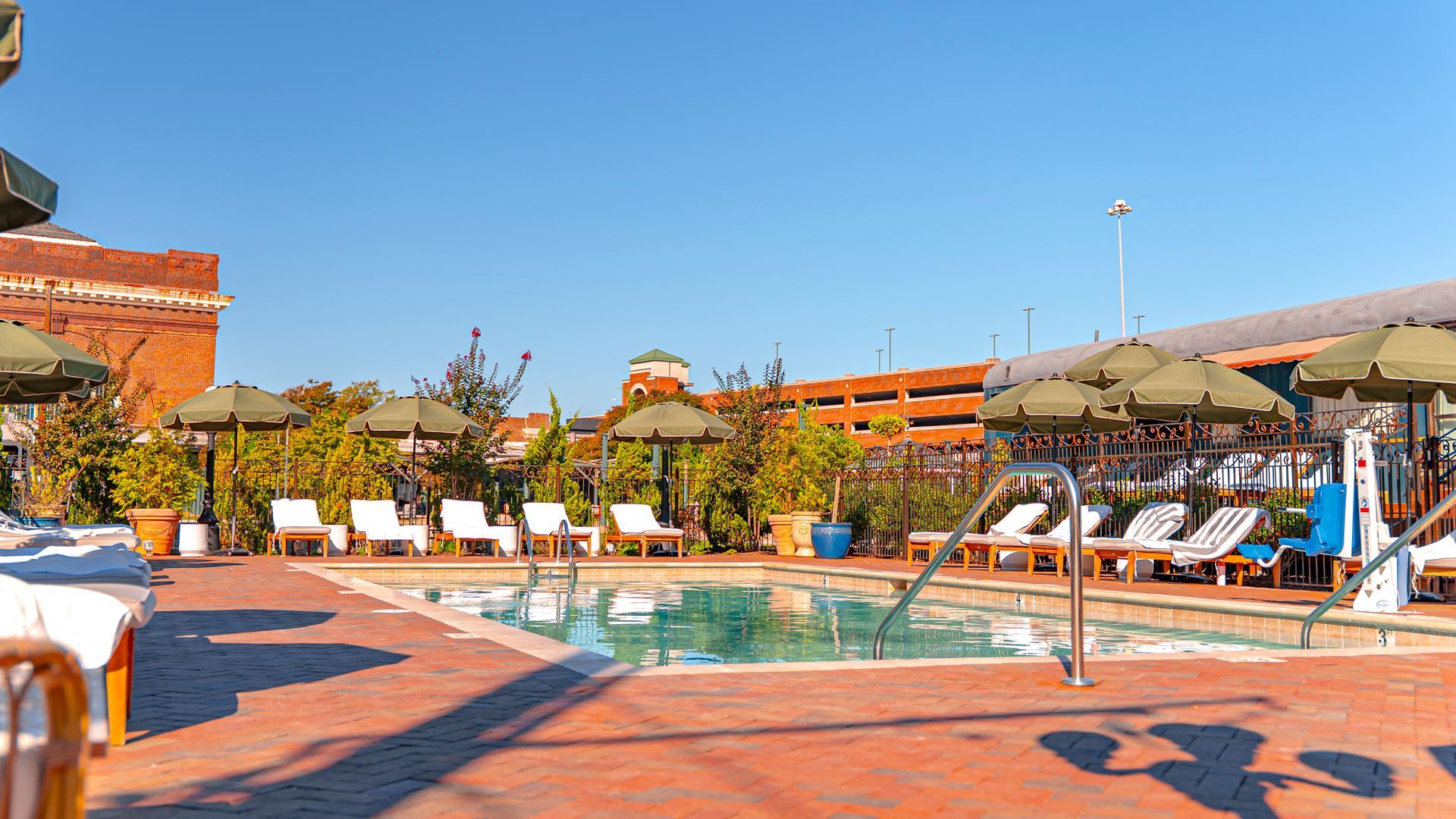 Rooftop pool with lounge chairs, umbrellas, brick patio, and a clear blue sky.