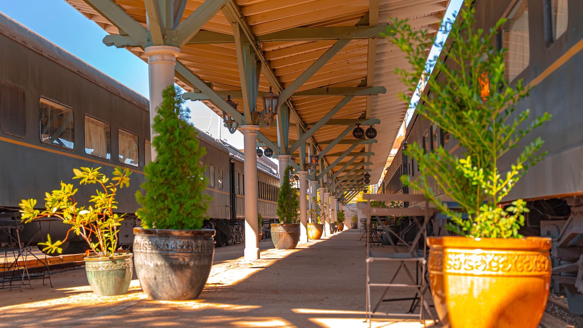 Train platform with parked trains, potted plants, and covered walkway.