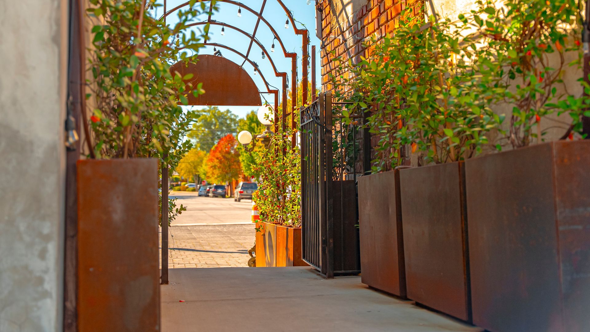 Pathway entrance with metal archway and planters leading to a street.