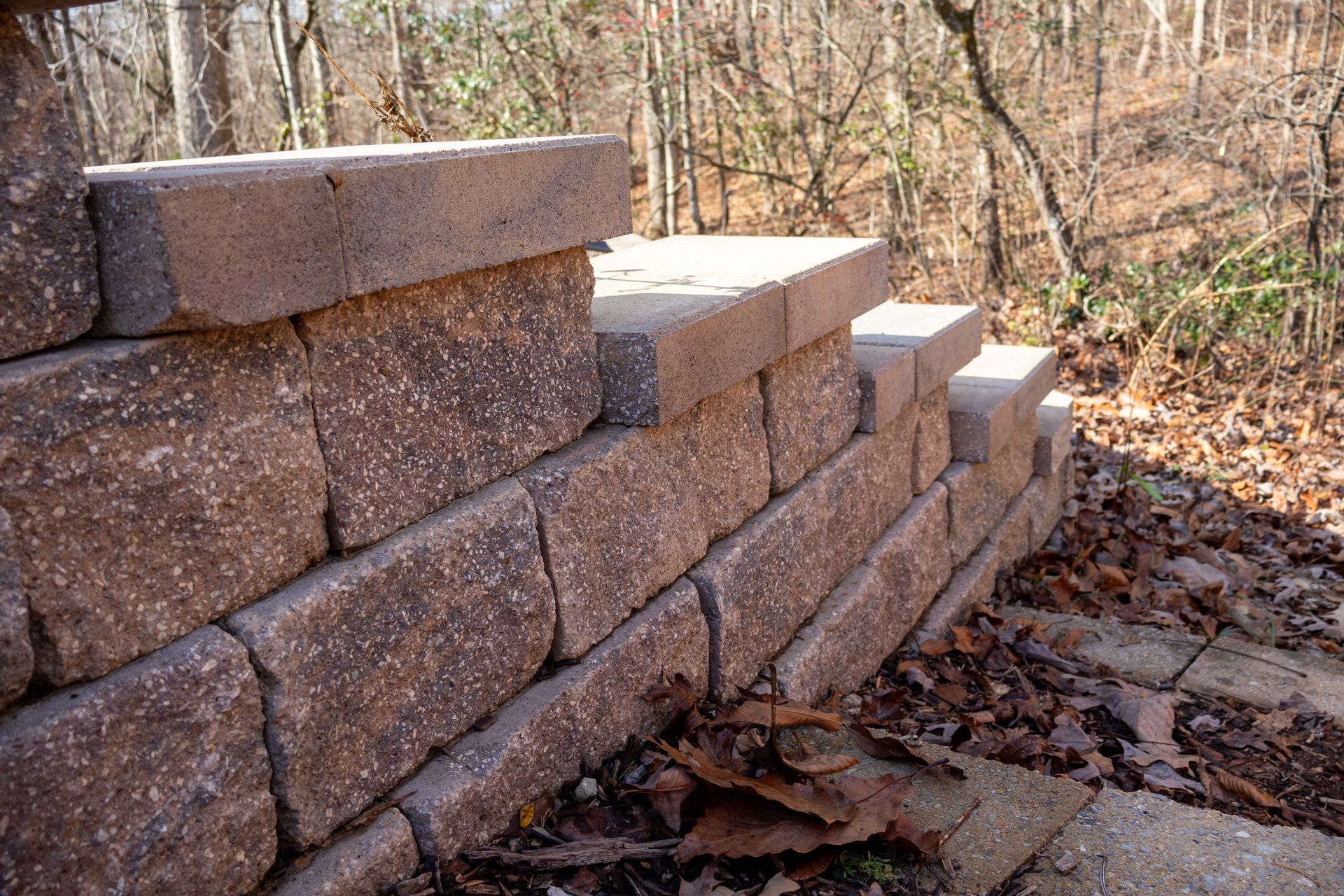 Stone retaining wall with steps outdoors; fall foliage and trees in background.