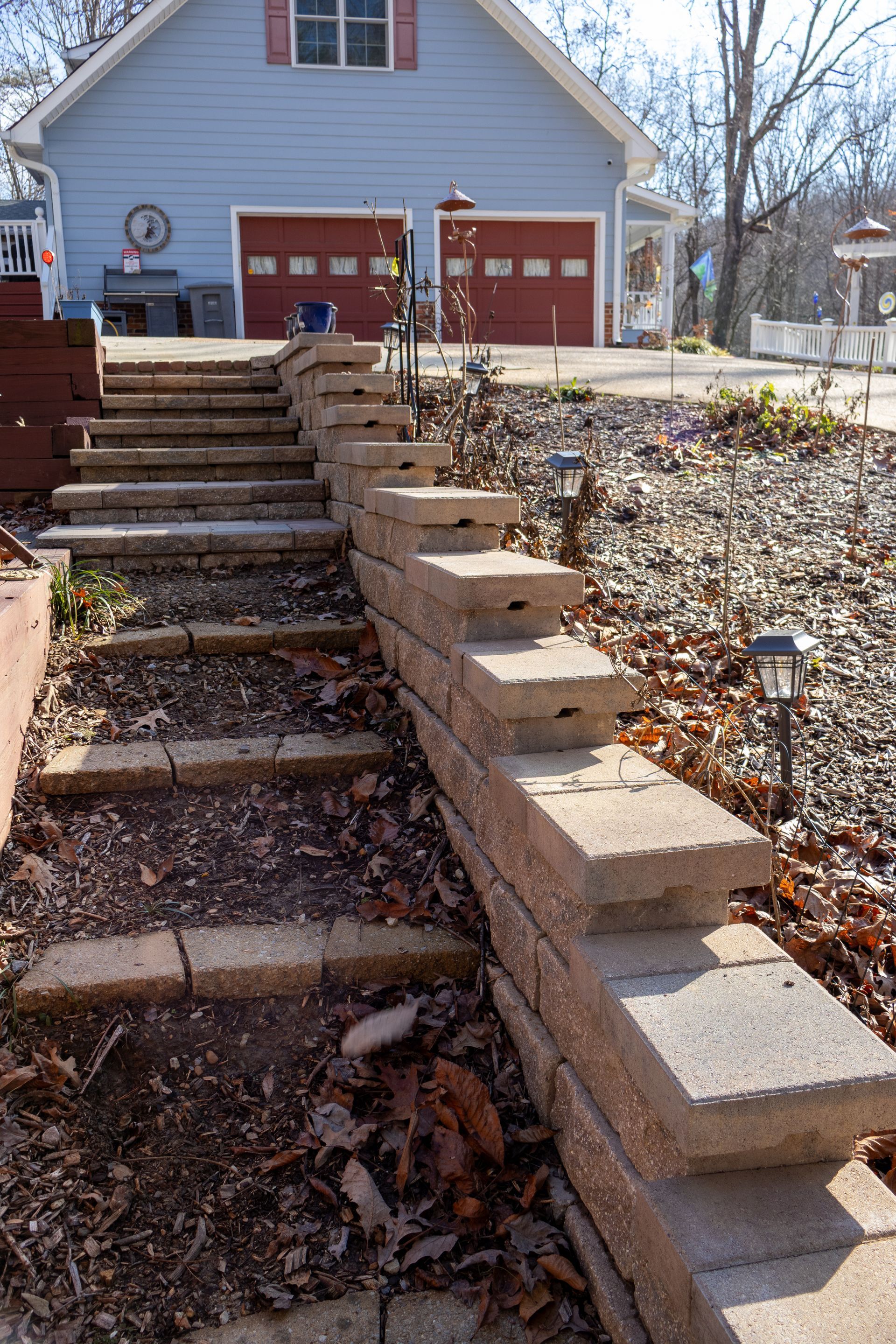 Stone steps with a retaining wall leading up to a blue house with red garage doors.