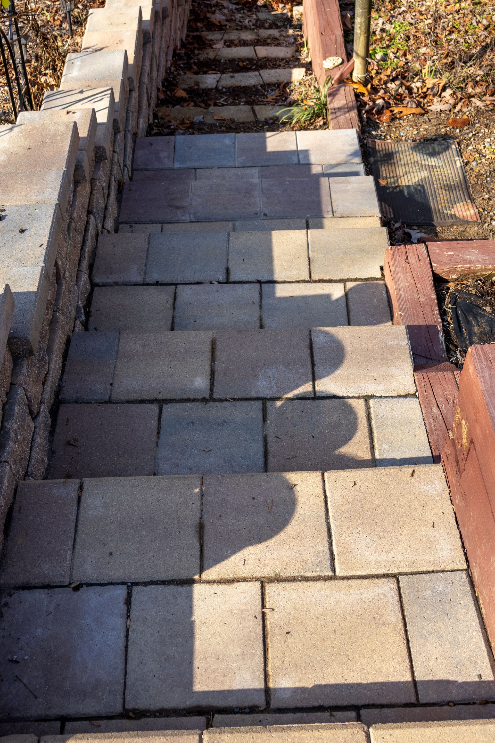 Stone steps descending outdoors, flanked by a brick wall and wooden railing. Shadows cast on steps.