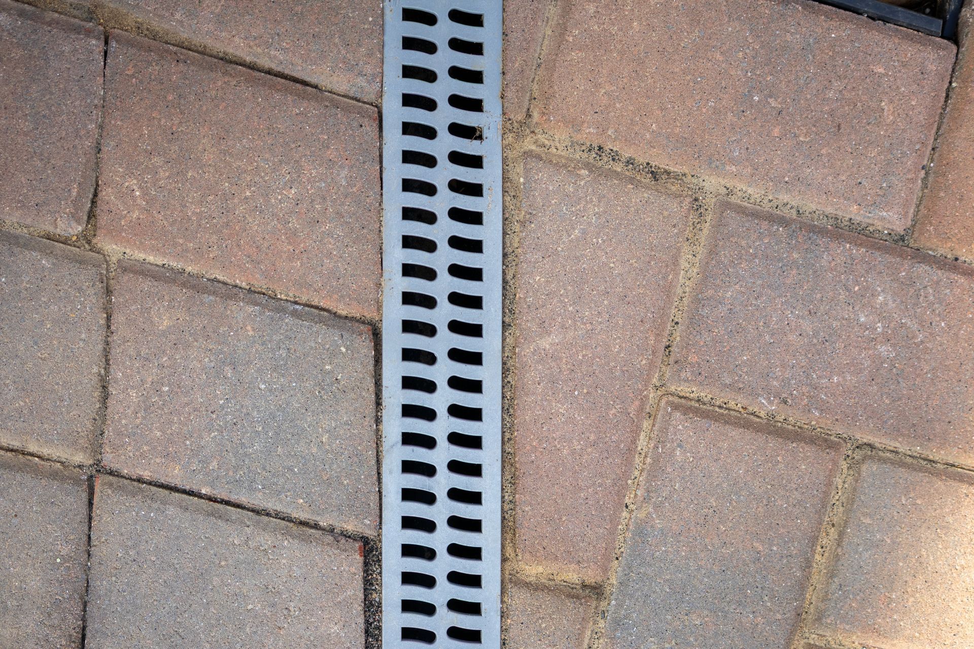 Gray drain strip set between brick pavers on a patio.