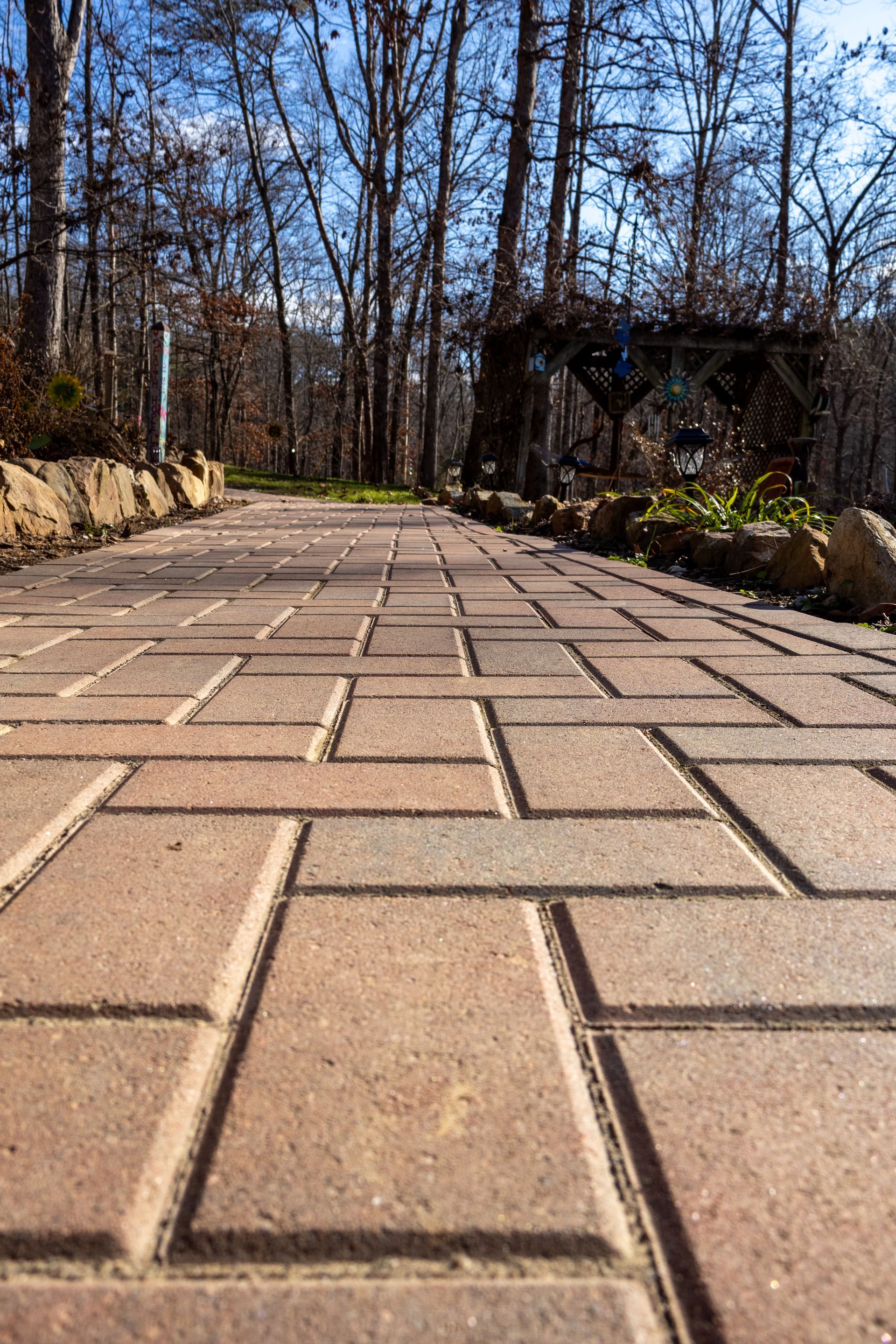 Brick pathway through a wooded area on a sunny day.