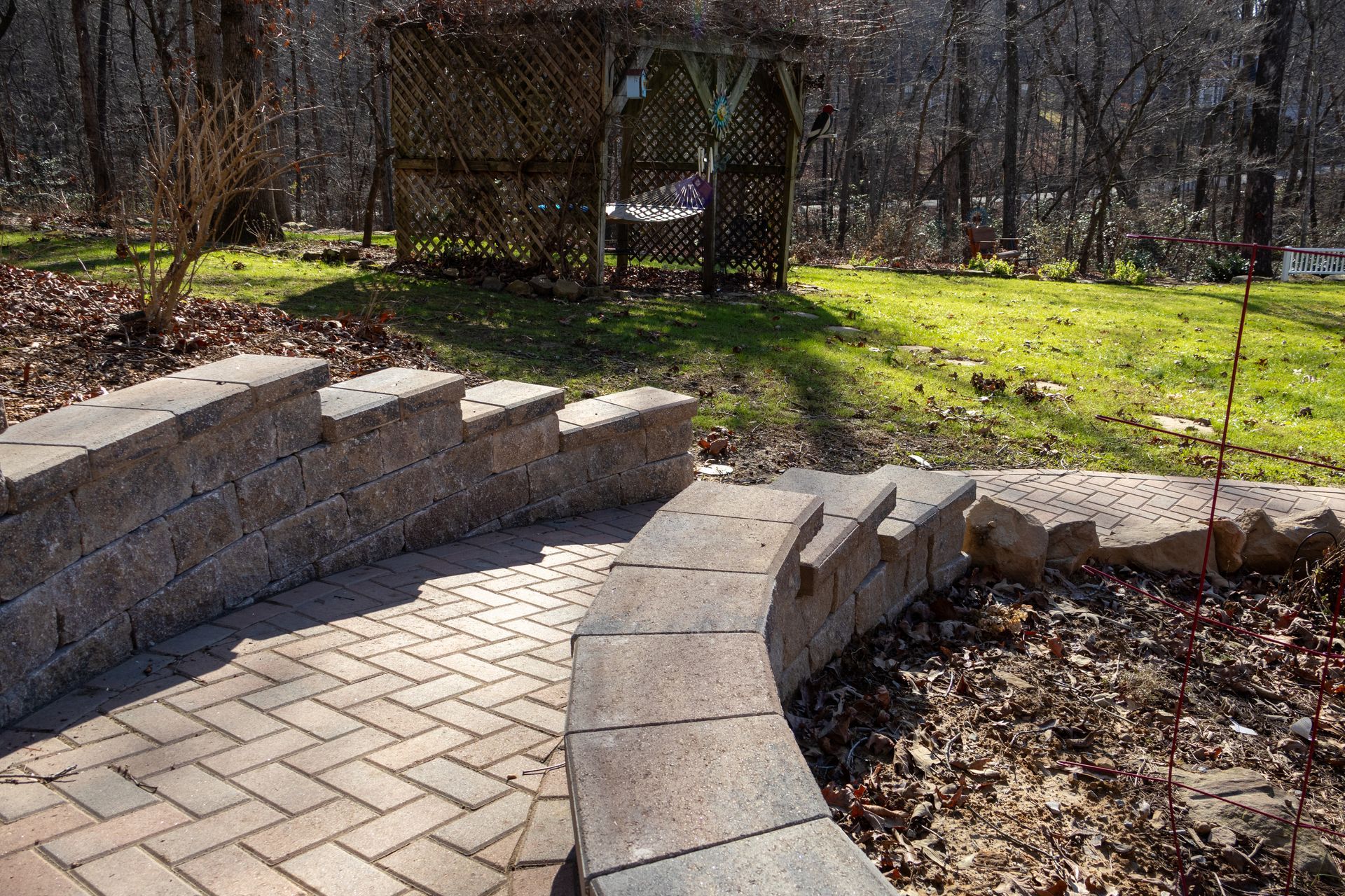 Curving brick pathway with retaining wall and wooden arbor in a sunny backyard setting.