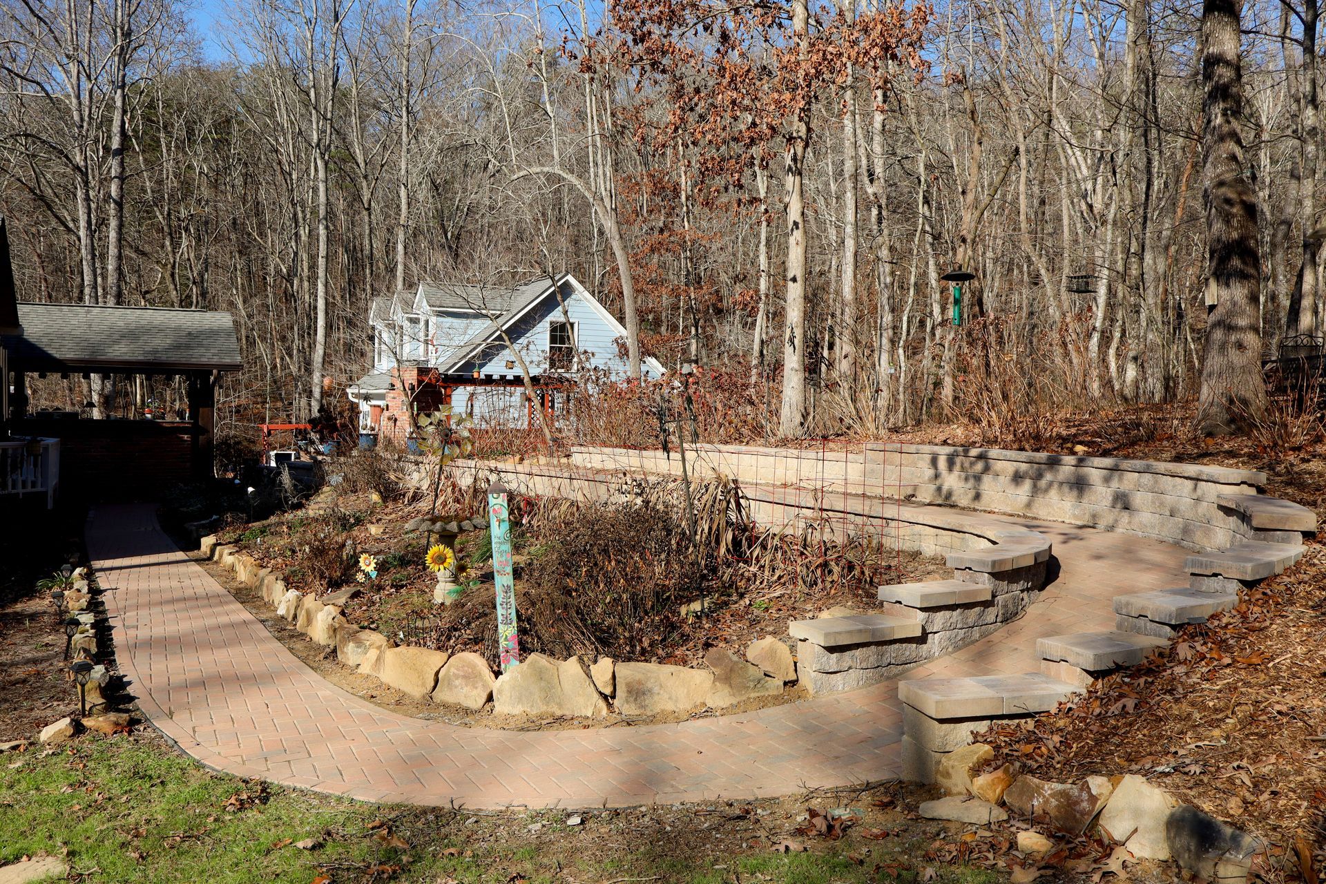 Stone pathway leading to a small house in a wooded area with a garden.