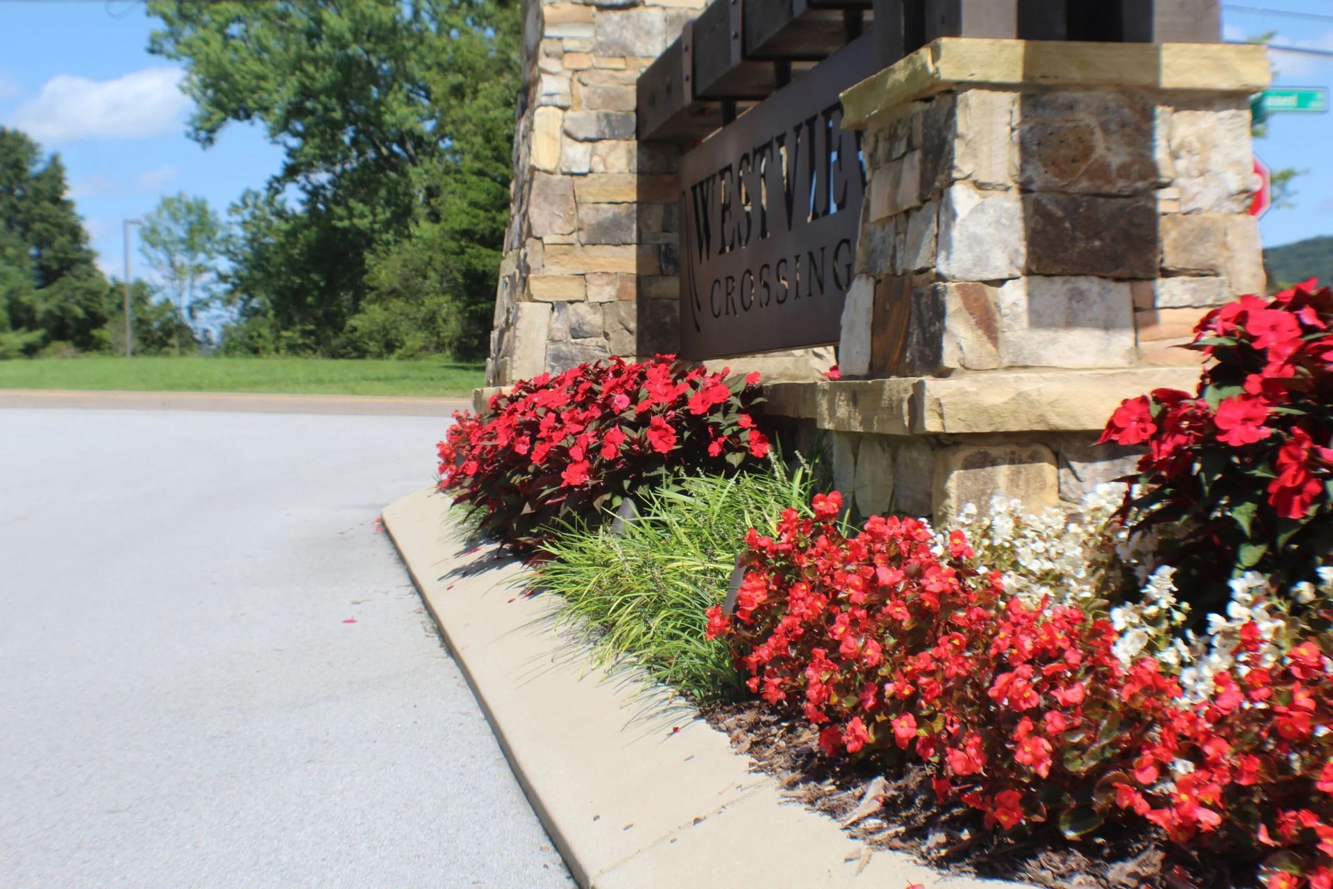 Sign for a community, framed by stone, with red flowers.