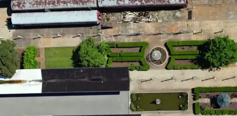 Aerial view of train cars, a formal garden with a fountain, trees, and buildings.