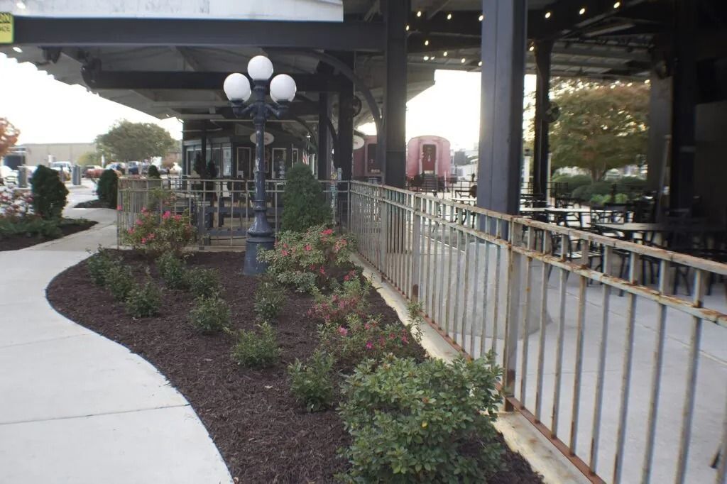 Outdoor patio with metal railing, landscaping, and a street lamp.