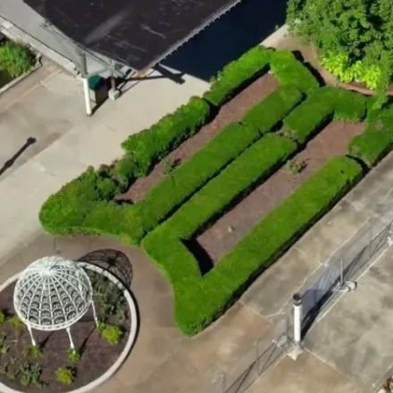 Overhead view of a green hedge maze next to a gazebo and building. Concrete walkways surround them.