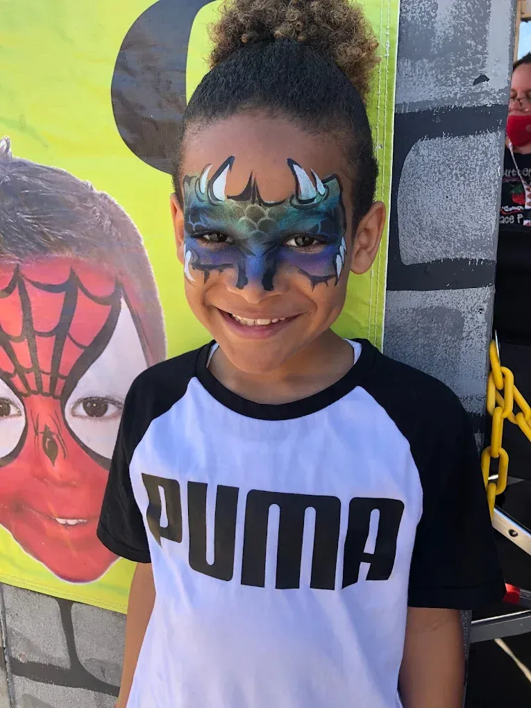 Child with blue face paint and a Puma shirt smiling in front of a colorful mural