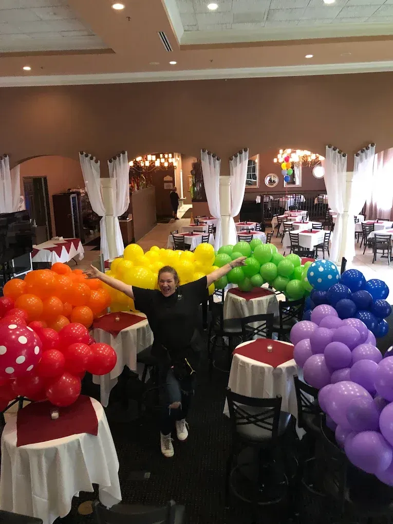 Person seated among colorful balloon displays in a banquet hall
