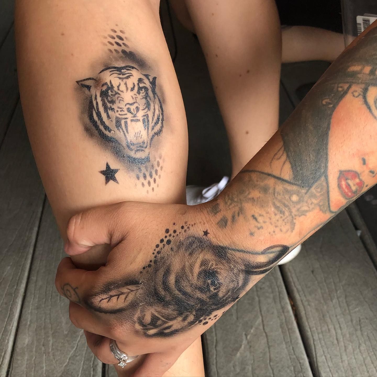 Two tattooed hands clasped, showing a tiger tattoo and a small star on a leg.