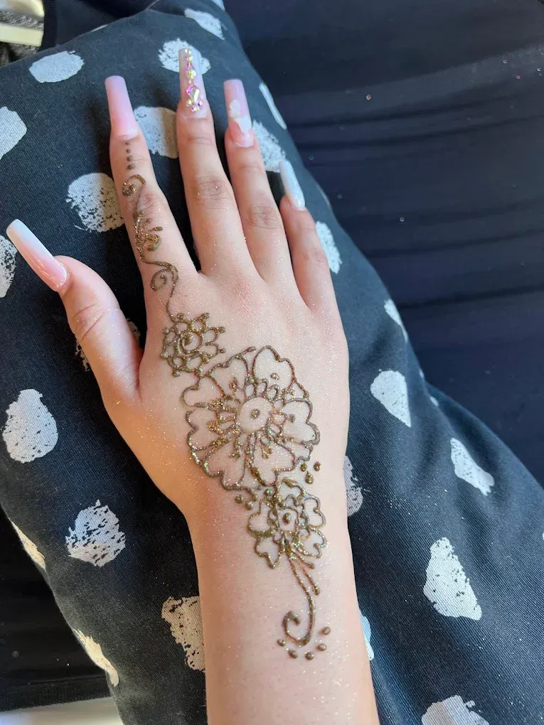 Hand with pink nails showing floral henna design on a dark patterned fabric background