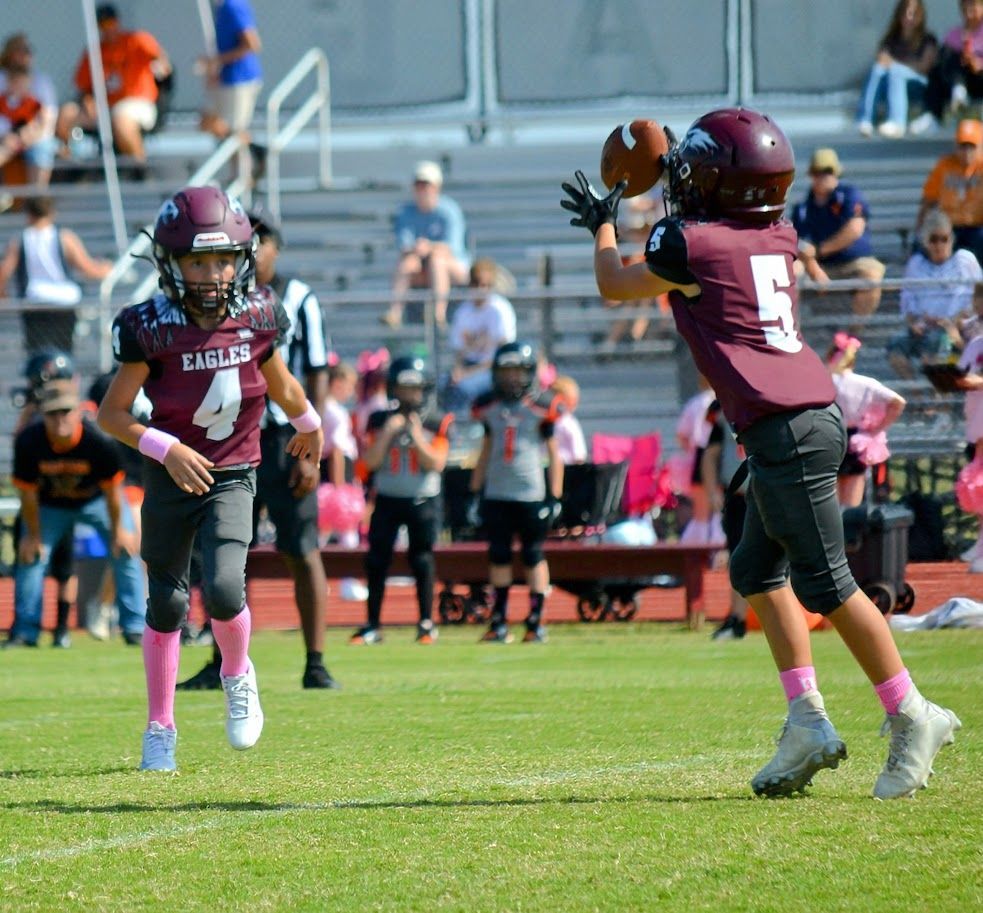Football player in maroon jersey holding ball, smiling, surrounded by teammates on a field.