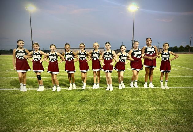 Cheerleader in red uniform performs a backbend on a green and red football field.