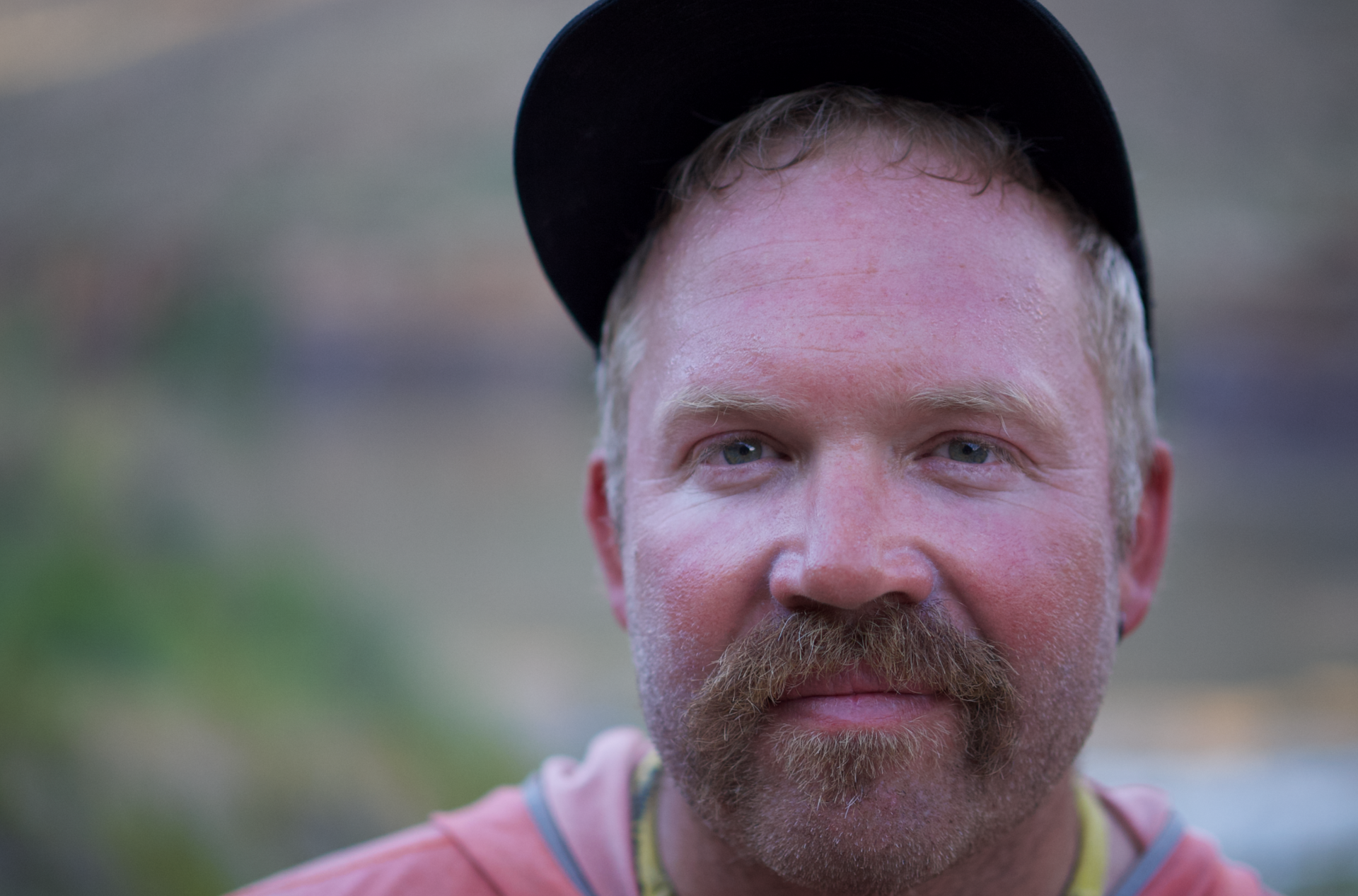 A man with a beard and hat is looking at the camera.