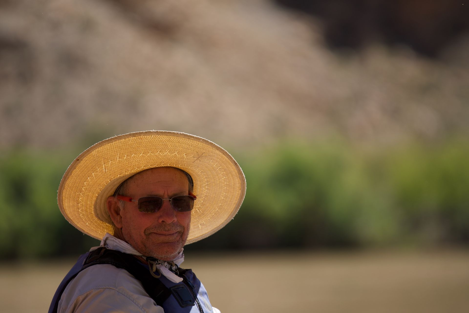 A man wearing a straw hat and sunglasses is standing in a field.