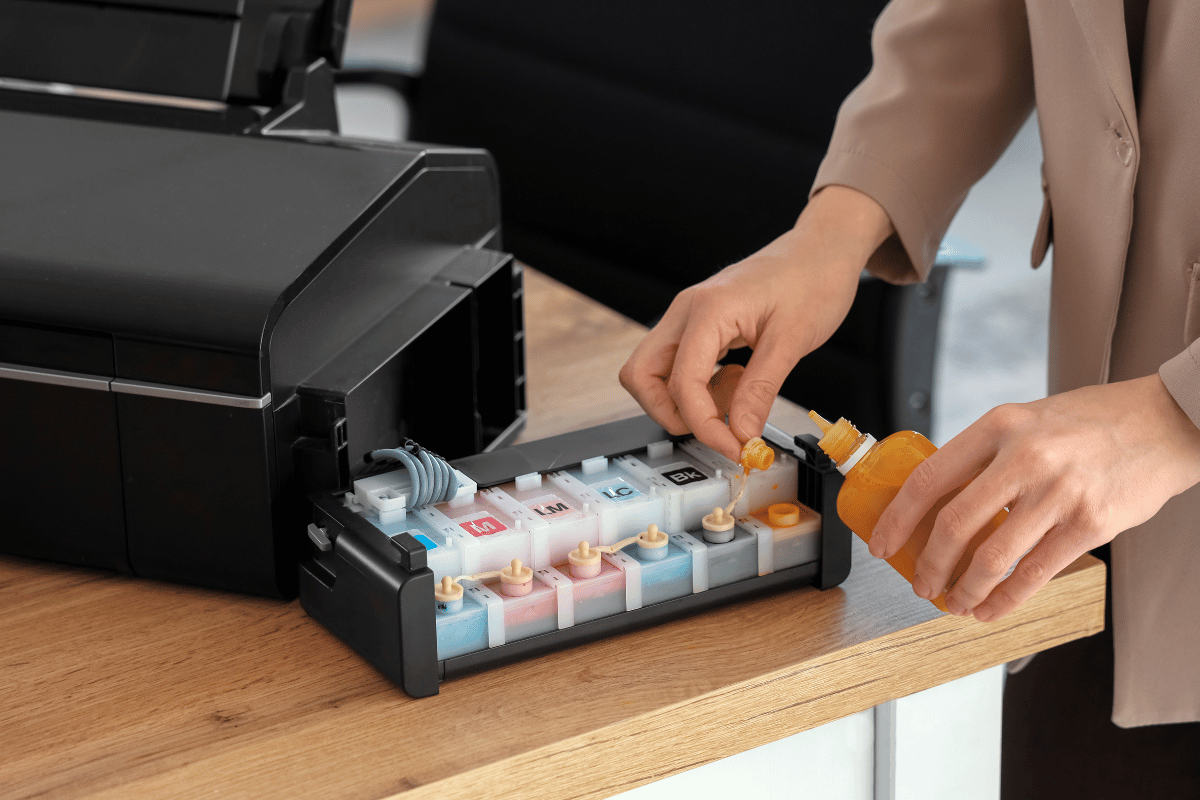 Hands loading colorful ink cartridges into a black printer tray on a desk