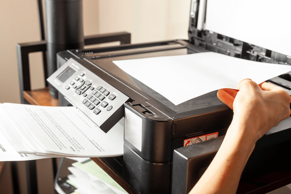 Hand placing paper on a printer/scanner as a sheet prints from the tray
