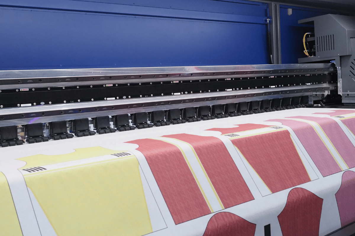 Large-format printer printing colorful striped fabric sheets with a blue machine overhead