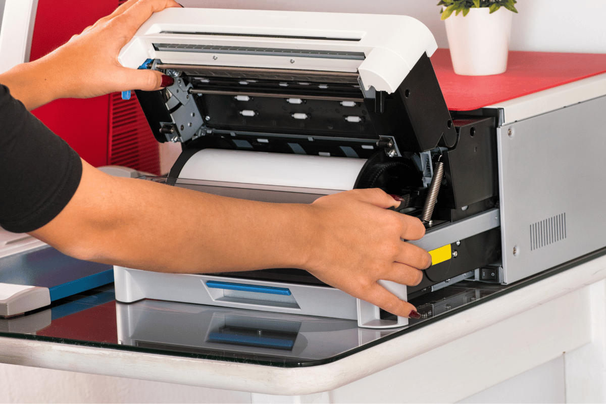 Person loading paper into an open office printer on a desk