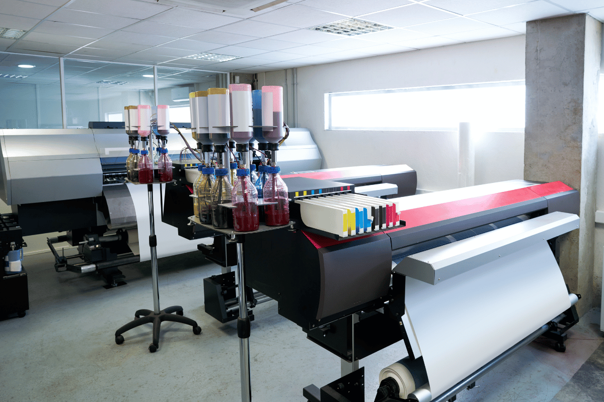 Large-format printer in a bright office, with paper rolls and colorful print materials nearby