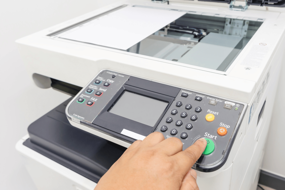 Hand pressing the green start button on a multifunction printer control panel