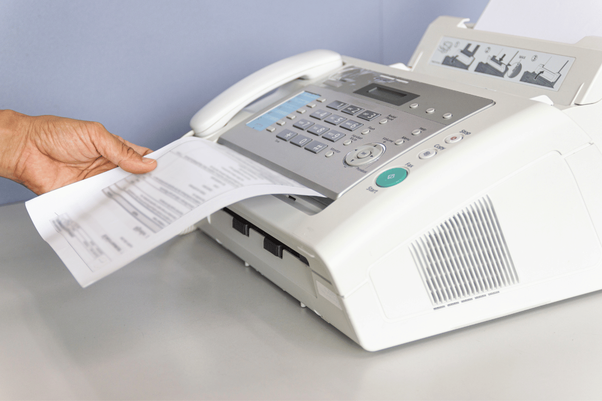 Hand placing a sheet into a white desktop fax machine printing a document