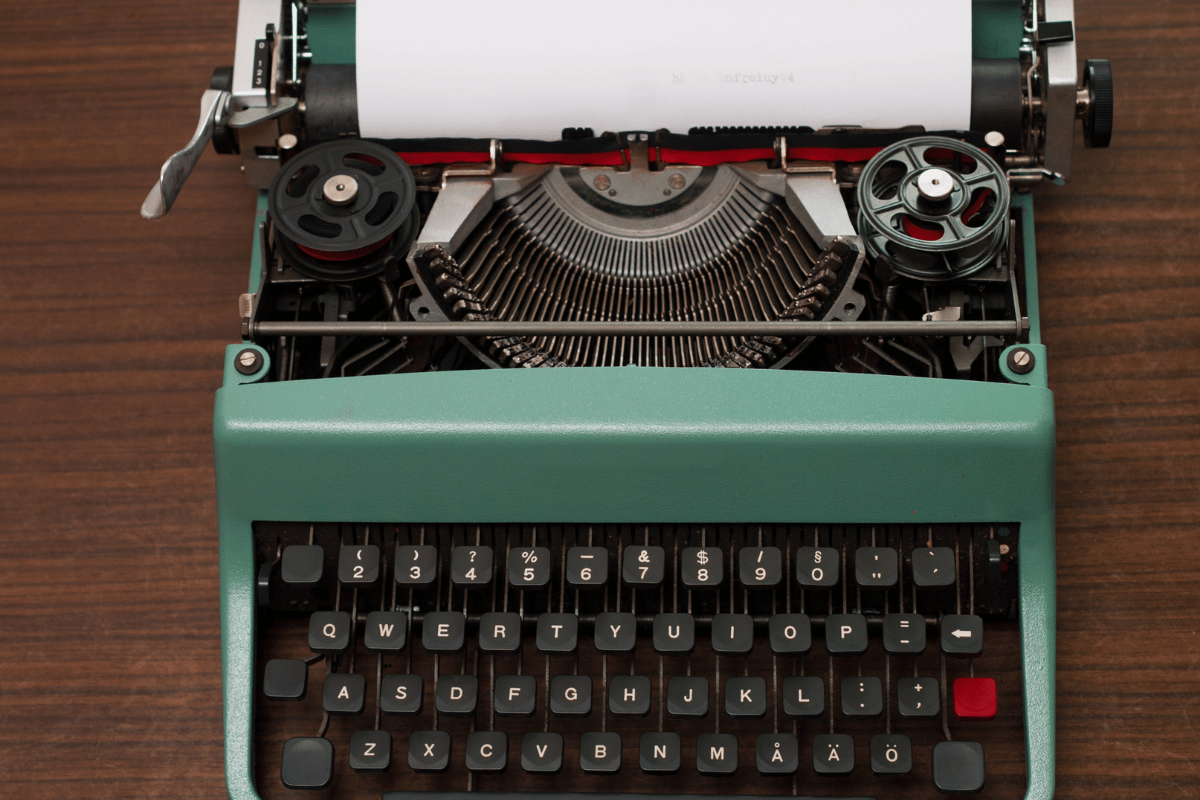 Vintage green typewriter with white paper loaded on a wooden table