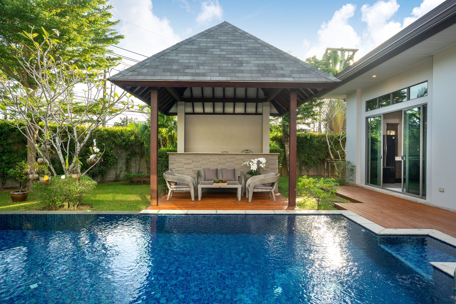 An outdoor pavilion in a residential home's backyard, sitting poolside with a comfortable furniture set