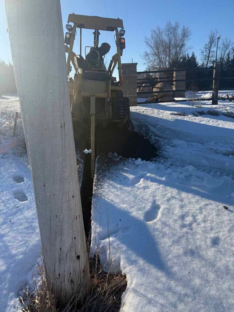 A yellow tractor drilling near a utility pole in a snowy field.