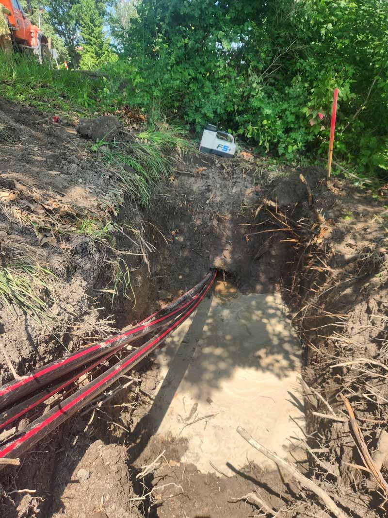Cables extending from a trench to a concrete pad, surrounded by dirt and vegetation.
