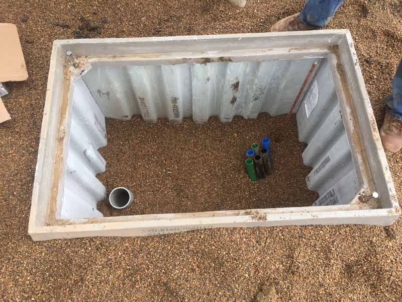 Open concrete utility box with gravel base and corrugated sides, outdoors.