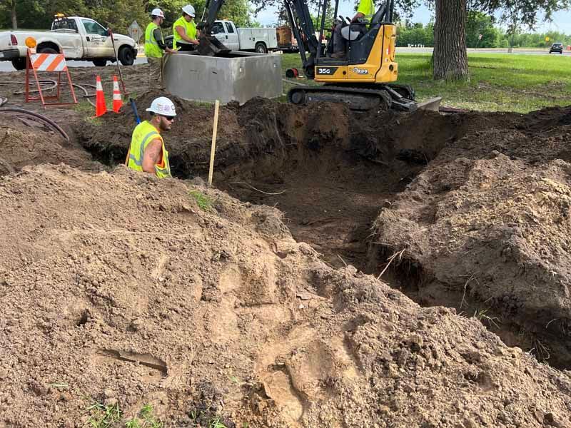 Construction workers excavating a ditch near a concrete structure, using machinery and hand tools.