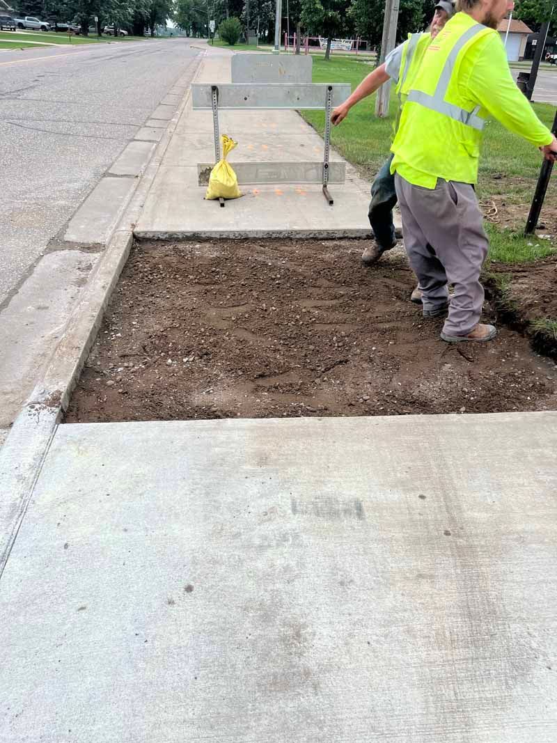 Workers in safety vests preparing a soil bed next to a sidewalk.