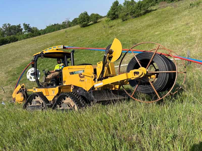 Yellow tracked machine laying cable on a grassy hillside.