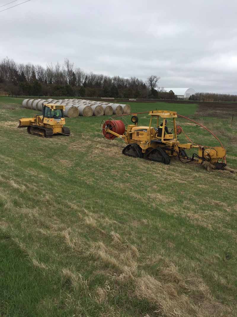 Two yellow tractors in a field with hay bales and an overcast sky.