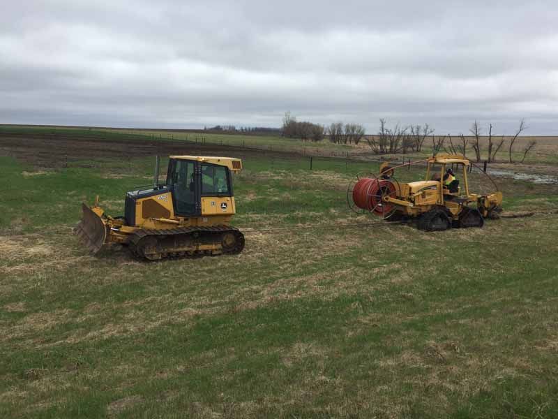 Two yellow construction vehicles in a grassy field under a cloudy sky.